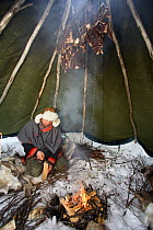 Saami herder hanging Reindeer (Rangifer tarandus) meat above a fire in his lavo (tent) to smoke it. Kautokeino, Finnmark, North Norway, March 2007.
