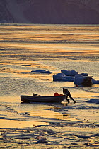 Inuit hunter manoeuvring his boat through newly formed sea ice at sunset. Inglefield Bay, Qaanaaq, Northwest Greenland, September 2008.