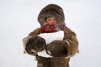 Nenets girl, warmly dressed in reindeer skin clothing, carrying snow to melt for water. Yamal, Northwest Siberia, Russia, February 2007. Editorial use only.