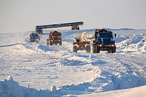 Trucks carrying large sections of gas pipe on a winter road near the Yurharovo gas field. Noviy Urengoi, Yamal, Western Siberia, Russia.