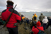 Man with rifle guarding photographers against Polar bears while they are photographing Walrus. Prins Karls Forland, Spitsbergen, Svalbard, Norway, June 2008.