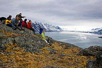 Walkers resting on a ridge of moss covered tundra high above Tinayre Bukta, Krossfjorden, Spitsbergen, Svalbard, Norway, June 2008.