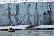 Tourists in a zodiac watching a waterfall tumble from the top of a glacier. Spitsbergen, Svalbard, Norway, June 2006.