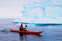 Eco tourist in a sea kayak paddling past an iceberg. Danco Island, Antarctica.