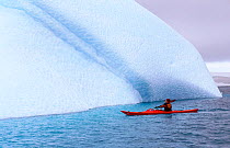 Eco tourist in a sea kayak paddling past an iceberg near Danco Island. Antarctic Peninsula