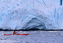 Eco tourist in a sea kayak paddling past a glacier near Port Lockroy, Antarctic Peninsula.