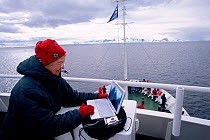 Photographer downloading from digital camera to  laptop on the deck of tourist ship, Antarctica.