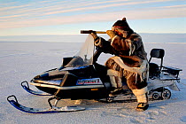 Inuk in fur clothing steadying his telescope on snowmobile while out hunting. Igloolik, Nunavut, Canada, 1995.