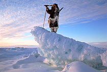 Inuk in fur clothing on ice ridge, looking for seals with telescope. Igloolik, Nunavut, Canadian Arctic, 1995.
