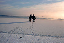 Two Inuit hunters leaving footprints in the snow-covered ice. Baffin Island, Nunavut, Canada, 1990.
