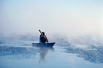Inuit hunter paddling a floe edge boat through frost smoke while seal hunting at the ice edge near Igloolik, Nunavut, Canada, 1990.