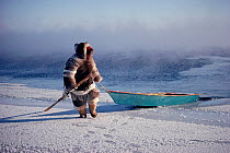 Inuit man hauling his floe edge boat while seal hunting at the ice edge. Igloolik, Nunavut, Canada, 1990.