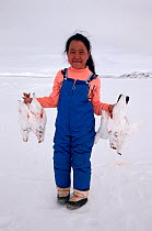 Inuit girl holding Rock ptarmigans (Lagopus mutus) that her father has shot for food. Baffin Island, Nunavut, Canada, 1992.