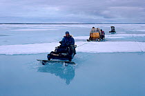 Inuit hunters travelling by snowmobile across wet sea ice during the summer thaw. Igloolik, Nunavut, Canada, 1992.