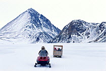 Inuk driving his snow scooter with a family box on the sled, Pond Inlet, Nunavut, Canada, 1999.