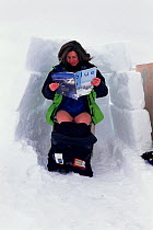 Woman using an outdoor toilet screened from the wind by a wall of snowblocks. Nunavut, Canada, 1999.