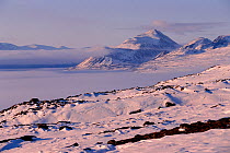 Snow covered tundra with Mount Herodier and Bylot Island shrouded in mist over Pond Inlet. Nunavut, Canada, 1999.