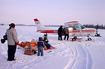 Cree family watching supplies arrive in small plane on the lake ice. Quebec, Canada, 1988.