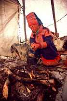 Sami herder cooking over fire in his tent during spring migration, Norway, 1985.