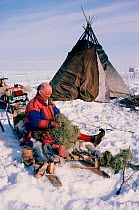 Sami herder stuffing boots with grass to keep his feet warm. Kautokeino, North Norway, 1985.