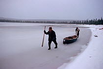 Two Innu hunters hauling canoe along edge of frozen lake. Labrador, Canada, 1997.