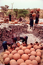 Dogon women placing pots in firing pit with rims touching sides to conduct the heat. Tireli, Mali, West Africa, 1981.