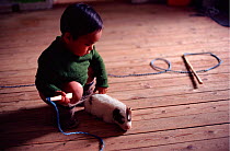 Inuit child with whip and Husky (Canis familiaris) puppy. Qeqertat, Northwest Greenland, 1980.