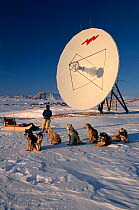 Inuit hunter and Huskies (Canis familiaris) by parabolic antenna at Savissivik, Northwest Greenland, 1996.