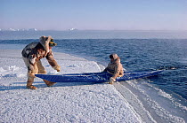 Inuk helping hunting companion launch kayak from floe edge. Northwest Greenland, 1986.