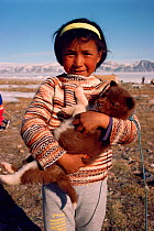 Young Inuit girl from Siorapluk holding Husky dog (Canis familiaris) puppy, Northwest Greenland, 1989.