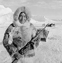 Inuit hunter in Caribou / Reindeer skin qulittaq (parka) holding rifle on hunting trip in spring. Thule, Northwest Greenland, 1971.