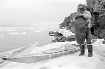 Inuit hunter inflating sealskin avatak (float) on ice foot by his kayak. Qeqertat, Thule, Northwest Greenland, 1977.