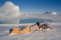 Inuit hunter shooting seal from behind concealing white linen screen. Northwest Greenland, 1997