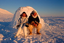 Warmly dressed Inuit couple sitting outside their igloo, Northwest Greenland, 1998.