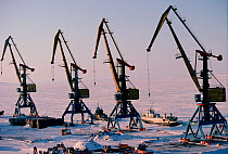 Boats frozen into sea ice beside harbour cranes in winter. Anadyr, Chukotka, Siberia, Russia, 1994.