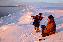 Two Chukchi boys hunting seals from snow covered shoreline. Dezhnovka, Chukotka, Siberia, Russia, 2004.