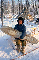 Evenk herder at winter camp in the forest, holding a pair of traditional Evenk Reindeer / Caribou skin covered skis. Surinda, Evenkiya, Central Siberia, Russia, 1997.