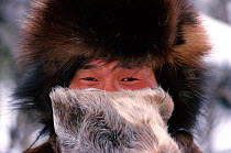Evenk man warming his nose with Reindeer skin mitten. Evenkiya, Siberia, Russia, 1997.