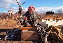 Elderly Even woman sewing tent at camp near Khailino. Koryakia, Kamchatka, Siberia, Russia, 1999.