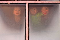 Girls looking through a window from inside their home in Verkhoyansk, Yakutia ,Siberia, Russia, 1999.