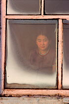 Girl looking through frosted window from inside her home in Verkhoyansk, Yakutia, Siberia, Russia, 1999.