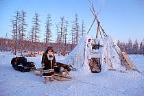 Evenk woman standing by traditional reindeer herders' winter tent (Tordok). Kusur, North Yakutia, Siberia, Russia, 2001.