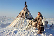 Nenets woman carrying an Arctic hare (Lepus arcticus) outside winter tent on the tundra. Gydan, Western Siberia, Russia, 2000.
