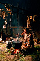 Nenets girl stirring pot of Reindeer stew over open fire inside tent. Yamal, Siberia, Russia, 1993.