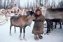 Nenets boy feeding bread to Reindeer / Caribou yearling (Rangifer tarandus) at winter camp. Yamal, Siberia, Russia, 1996.