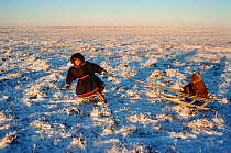 Nenets boy pulling younger child on a sled. Yamal, Western Siberia, Russia, 2001.