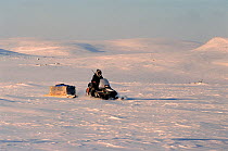 Inuit hunter driving his snowmobile across the tundra during hunting trip. George River, North Quebec, Nunavik, Canada, 1998.