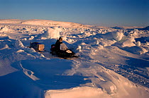 Inuit hunter driving his snowmobile across tidal ice during hunting trip. George River, North Quebec, Nunavik, Canada, 1998.