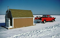 Truck moving fish house to better site on the lake. Mille Lacs Lake, Minnesota, USA, 1985.