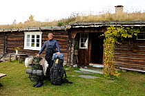 Laurent Joffrion with two rucksacks, standing outside traditional building with grass roof, Forollhogna National Park, Norway, September 2008
